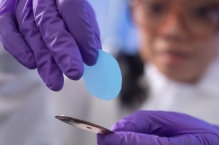 A scientist holds up a thin blue circular membrane. 