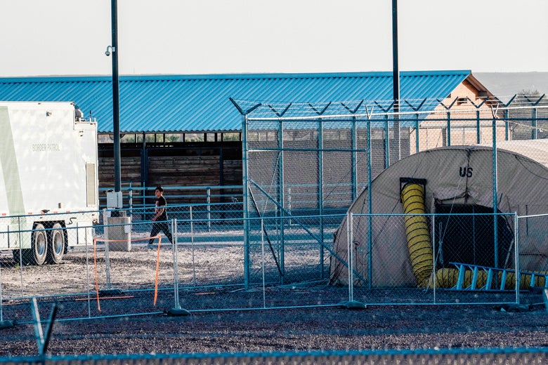 A tent and barrack behind barbed wire fencing.