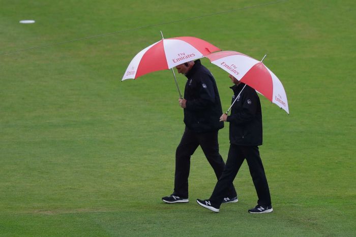 Umpires walk across the field with umbrellas