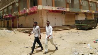 A group of men walk past a row of closed up shops in Khartoum's twin city, Omdurman