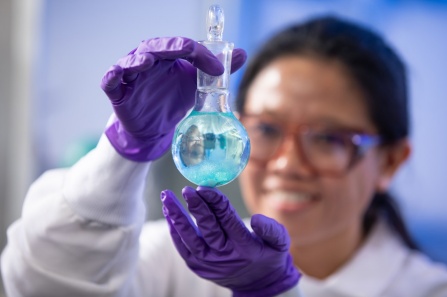 A scientist holding a vial filled with light blue liquid.