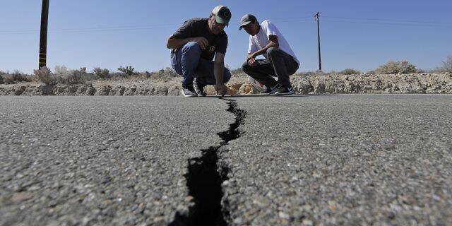 Ron Mikulaco, left, and his nephew, Brad Fernandez, examine a crack caused by an earthquake on highway 178 outside Ridgecrest, Calif. (AP Photo/Marcio Jose Sanchez)