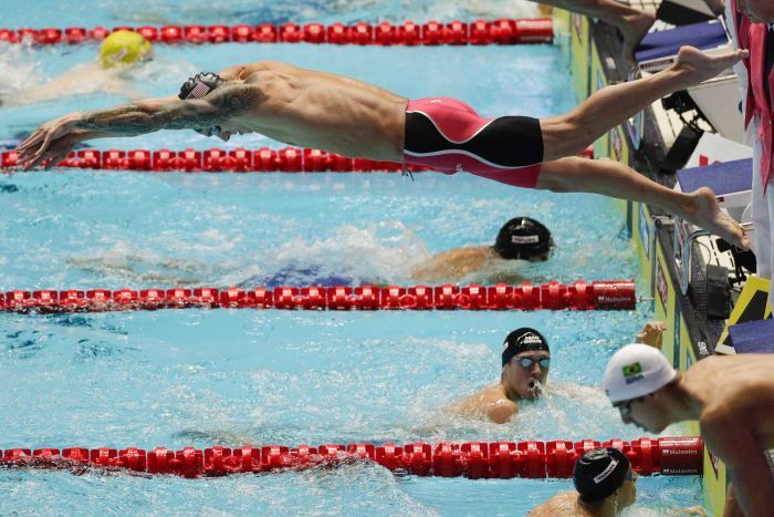 United States Caeleb Dressel dives into the pool as others swim in neighbouring lanes.