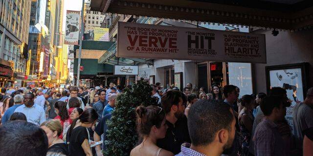 Theatergoers gather under darkened marquees on Broadway.