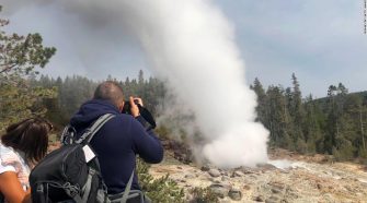 Tourists watch the Steamboat Geyser erupt on August 22, 2018, in Yellowstone National Park.