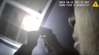 Bodycam still sows an officer with a torch and gun facing a window