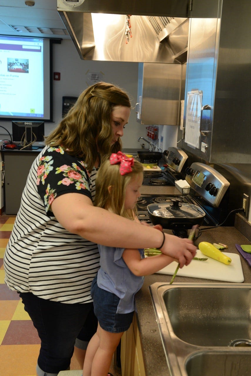 A parent helps her child chop and cook vegetables for a healthy meal.
