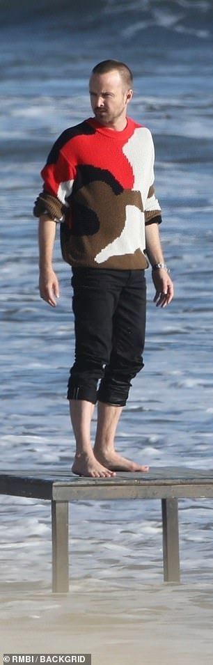 Beach look: Dressed down in a red, white, brown and black coloured jumper and black jeans, the star looked relaxed and happy as he worked in front of the camera