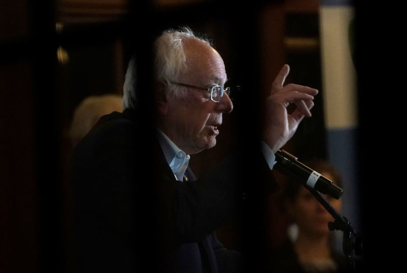 Bernie Sanders speaking into a microphone and gesturing with his hand.