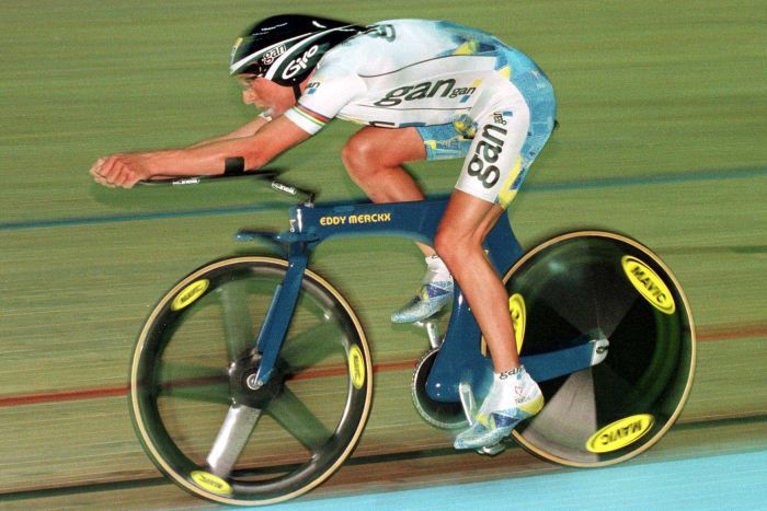 Chris Boardman cycles on a track with his arms well out in front of him on a prototype track bike