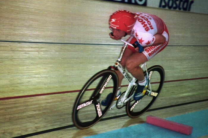 A cyclist rides a bike with his arms hunched next to him on a wooden track