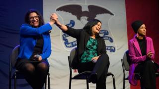 Rashida Tlaib high-fives Pramila Jayapal, while sitting next to Ilhan Omar, on stage at the event in Iowa