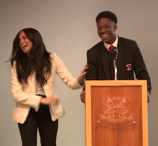 Pictured: Meghan smiles as Aker speaks during a school assembly in support of International Women's Day. Aker broke protocol and kissed Meghan on the cheek