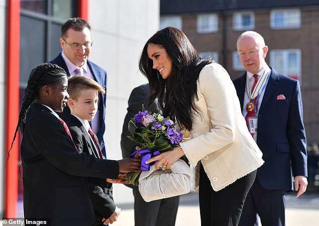 Pictured: radiant Meghan is greeted by staff and younger pupils who hand her flowers