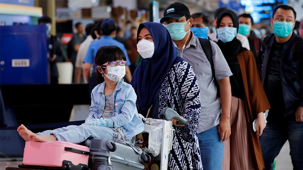 A girl wearing a protective face mask and synthetic gloves sits on luggages as she queues for temperature checking amid the spread of coronavirus disease (COVID-19) at Halim Perdanakusuma airport in J