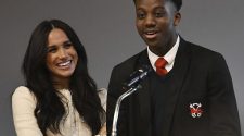 Pictured: the Duchess of Sussex smiles as head boy Aker Okoye address a school assembly during her surprise visit to the Robert Clack Upper School in Essex, March 6, 2020