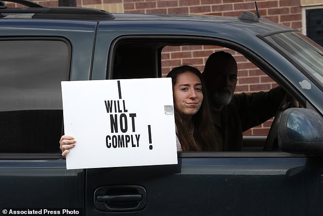 A passenger in a vehicle holds a sign during a protest at the State Capitol in Lansing, Michigan