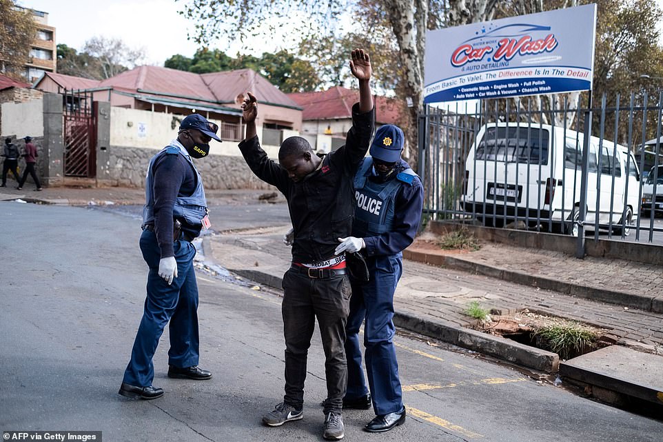 A man holds his hands above his head while being searched by South African Police Service (SAPS) officers in streets in Yeoville, Johannesburg
