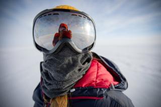 Person wearing a large pair of goggles - in icy Antarctic landscape... also a warm coat and scarf