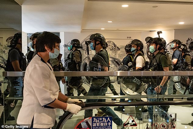 A cleaner wipes an escalator handle as riot police patrol during a demonstration in a shopping mall on May 10