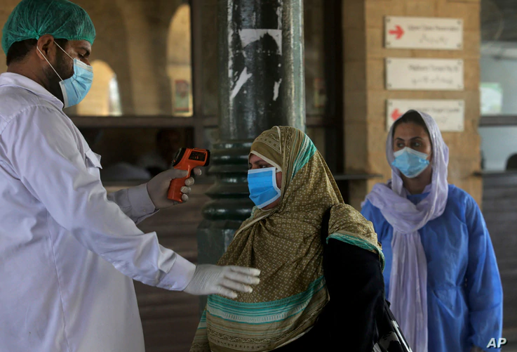 A railway worker checks the body temperature of a woman wearing a protective mask to help curb the spread of the coronavirus,…