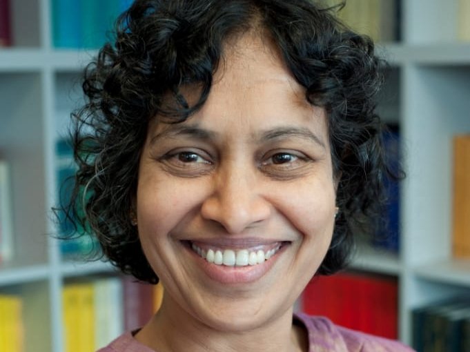 A smiling middle-aged woman of Indian origin wearing ethnic shift looks at camera in library.
