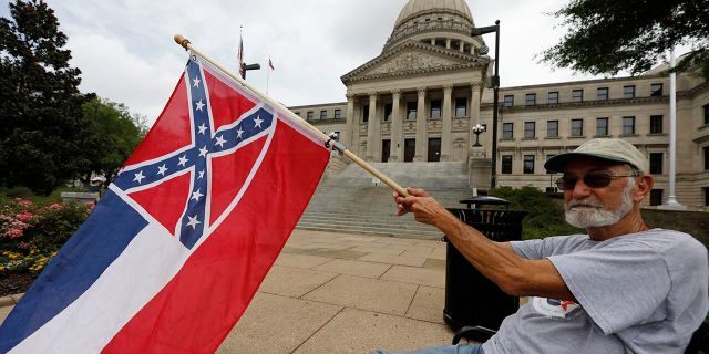 Larry Eubanks of Star waves the current Mississippi state flag as he sits before the front of the Capitol, Saturday, June 27, 2020, in Jackson, Miss. (Associated Press)