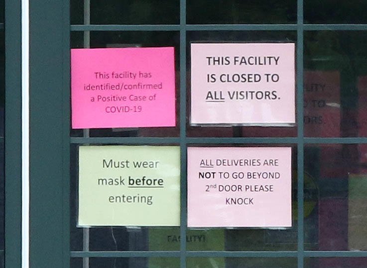 Signs posted on the front door of Pine Acres Rehab and Living Center in DeKalb Thursday afternoon warn that there are confirmed cases of COVID-19 in the building. Nine staff members and 31 residents at the facility have tested positive for COVID-19. One resident has died as a result of complications from the disease.