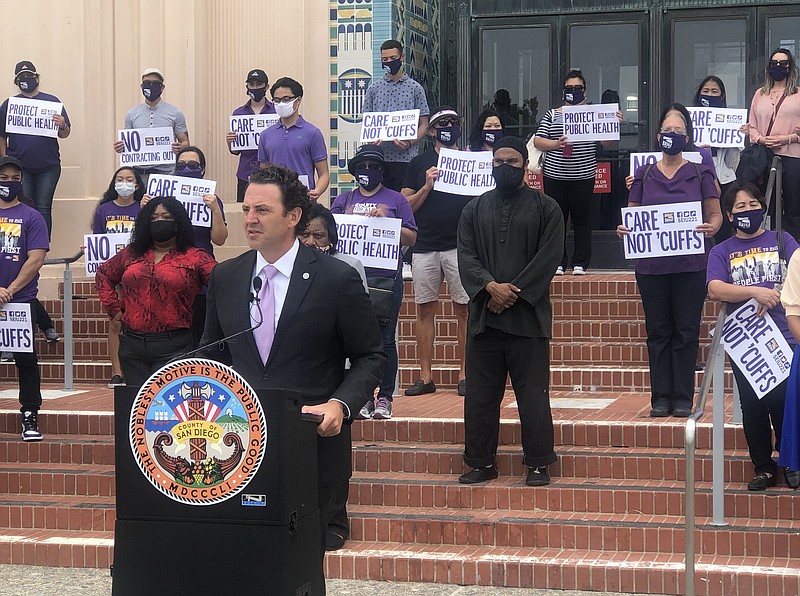 Sign-carrying union members stand behind San Diego County Supervisor Nathan F...
