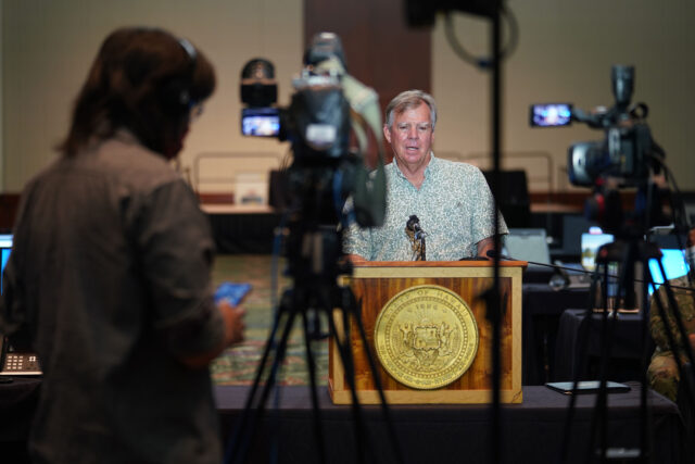 Department of Health Director Dr. Bruce Anderson speaks at podium with foreground, media cameras during contact tracing press conference held at the Hawaii Convention Center. August 19, 2020