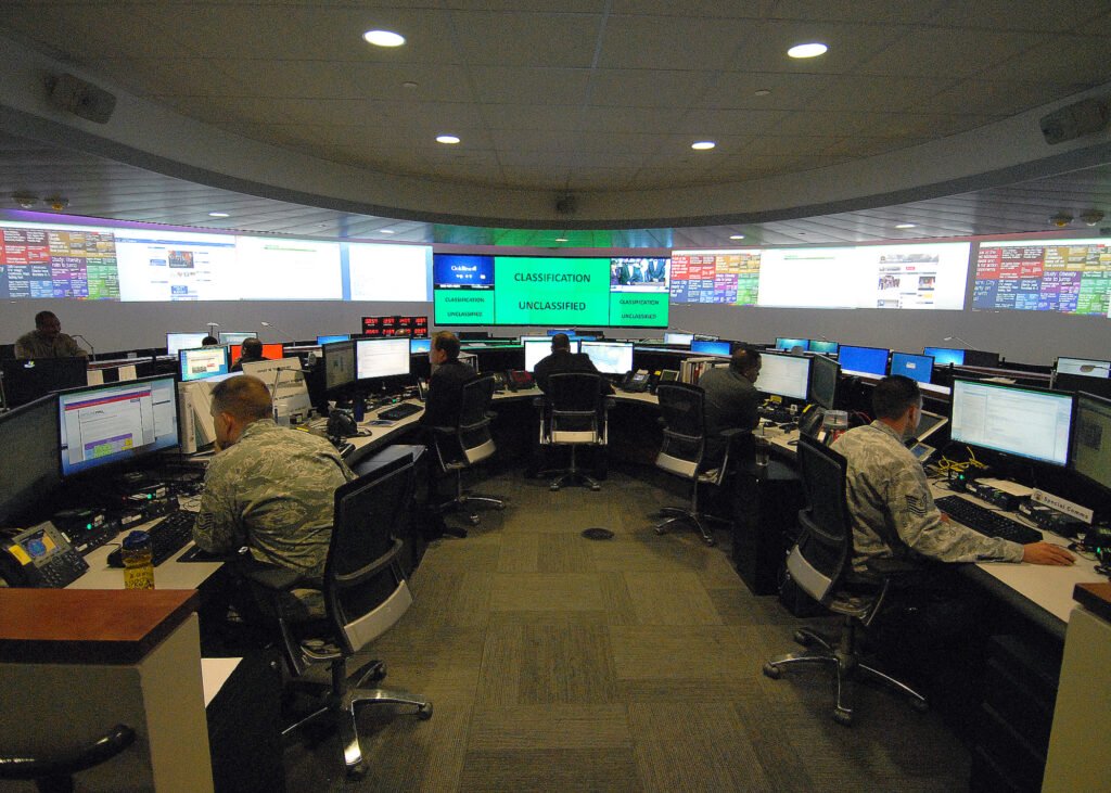 Several people in uniform sit in a room with many computers.