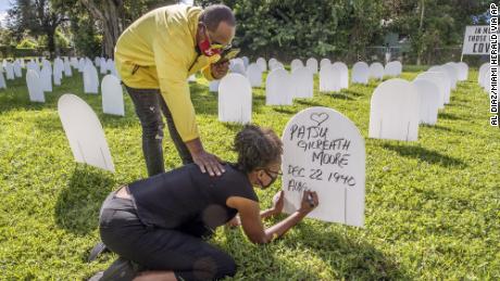 Rachel Moore honors her mother, Patsy Gilreath Moore, by writing her mother&#39;s name on a symbolic tombstone at Simonhoff Park in the Liberty City neighborhood of Miami on October 14.