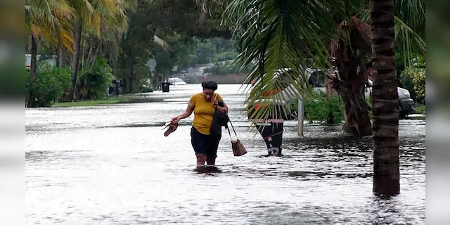 A woman crosses through floodwaters in the Melrose Place neighborhood in Fort Lauderdale, Fla., on Monday, Nov. 9, 2020.