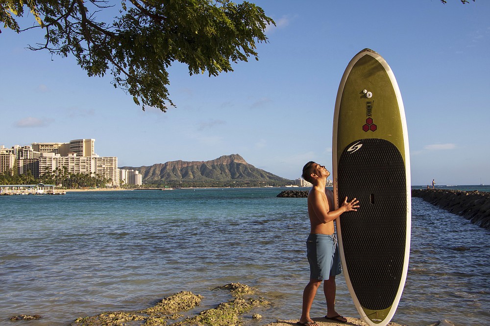 In this photo provided by Yoko Liriano, Bryant de Venecia poses for a photo with his paddleboard in Honolulu, Wednesday, Nov. 11, 2020. He started stand-up paddle-boarding when there were fewer tourists coming to Hawaii during the pandemic. He's among the Hawaii residents feeling ambivalence toward tourists returning now that the state is allowing incoming travelers to bypass a 14-day quarantine with a negative COVID-19 test. (Yoko Liriano via AP)