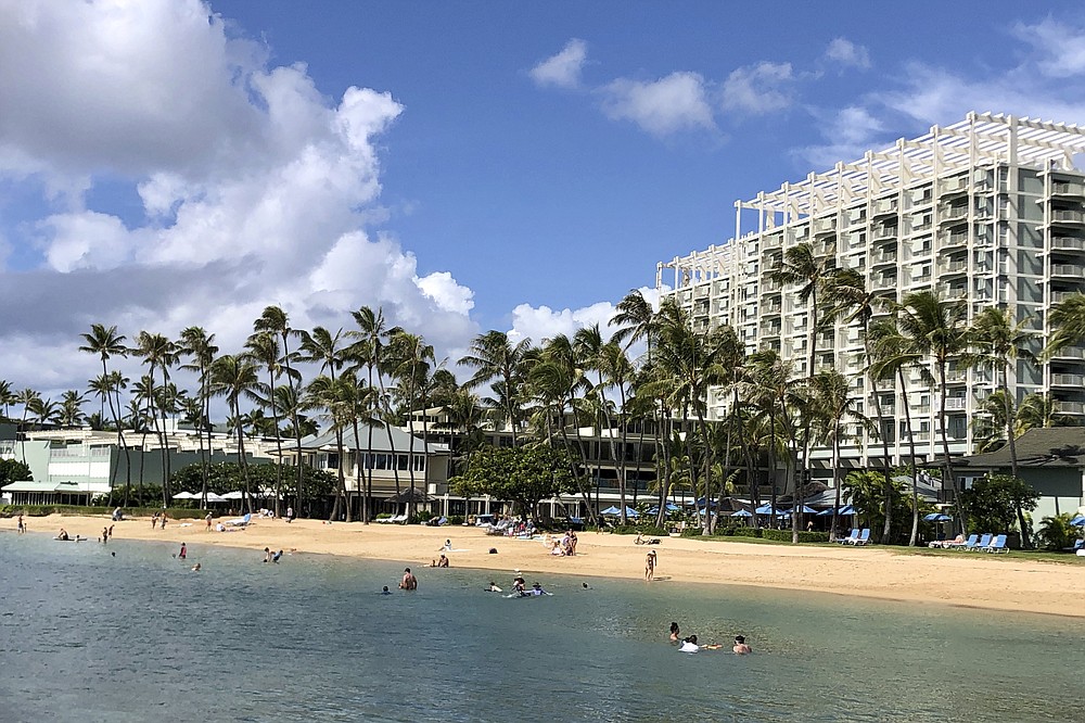 People are seen on the beach and in the water in front of the Kahala Hotel & Resort in Honolulu, Sunday, Nov. 15, 2020. Some locals in the tourism-dependent state have mixed feelings about the return of visitors during the pandemic after enjoying Hawaii beaches with dramatically fewer tourists since March. (AP Photo/Jennifer Sinco Kelleher)