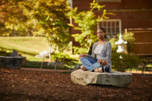 A student poses on a giant rock in UMW's Zen garden before COVID-19. Located between Trinkle and Mason halls, the garden is a peaceful outdoor spot for reflection and mindfulness. Photo by Adam Ewing.