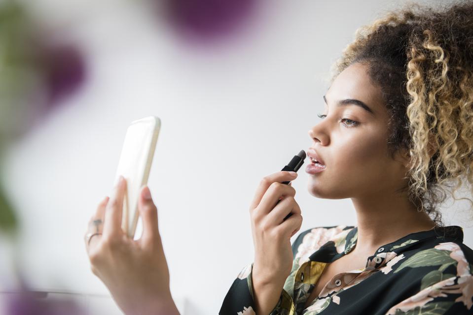 Woman holding cell phone applying lipstick