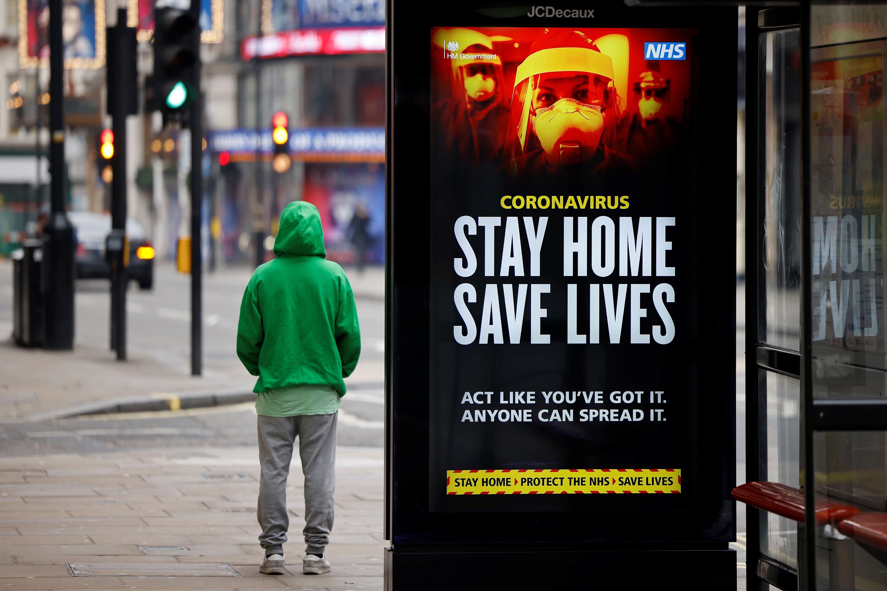 A man stands near signage promoting the UK's National Health Service message, "Stay Home, Save Lives" on a bus shelter in London on January 8.