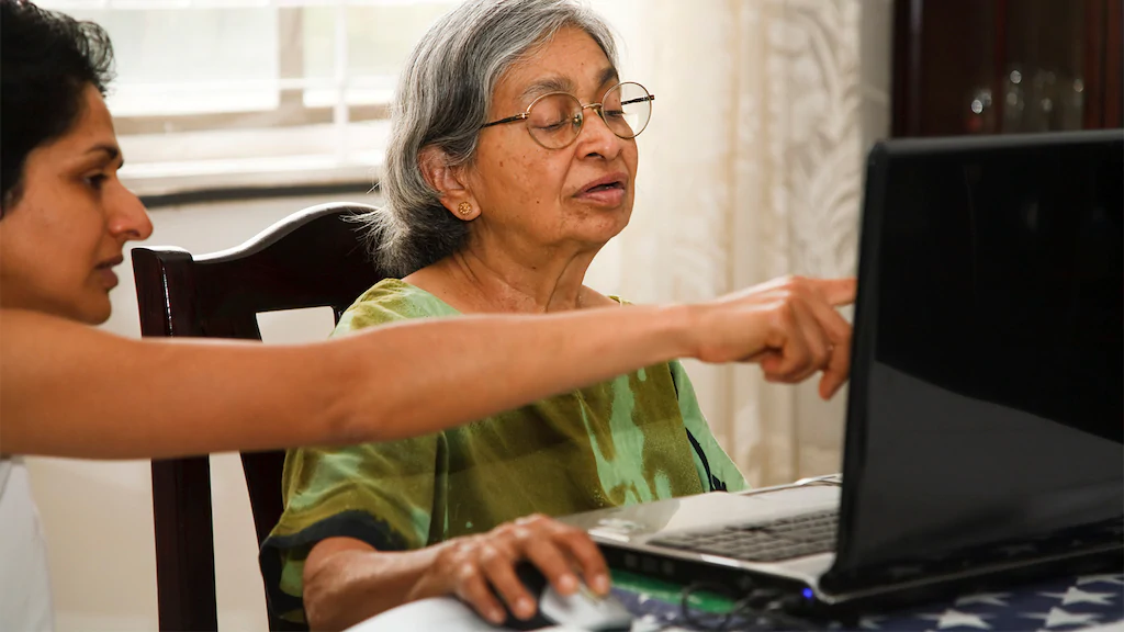 A woman helps her senior mother use a laptop