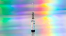 A syringe with vaccine. Rainbow background.