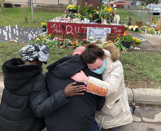 Jamesetta Collins (left), Samuel Howell and Katie Russell pay their respects Tuesday near a Daunte Wright memorial in Brooklyn Center, Minnesota. The memorial site, a giant, rust-brown sculpture of a clenched fist, is surrounded by flower bouquets, messages and candles. Wright, a 20-year-old Black man, was fatally shot by a police officer during a traffic stop on Sunday.