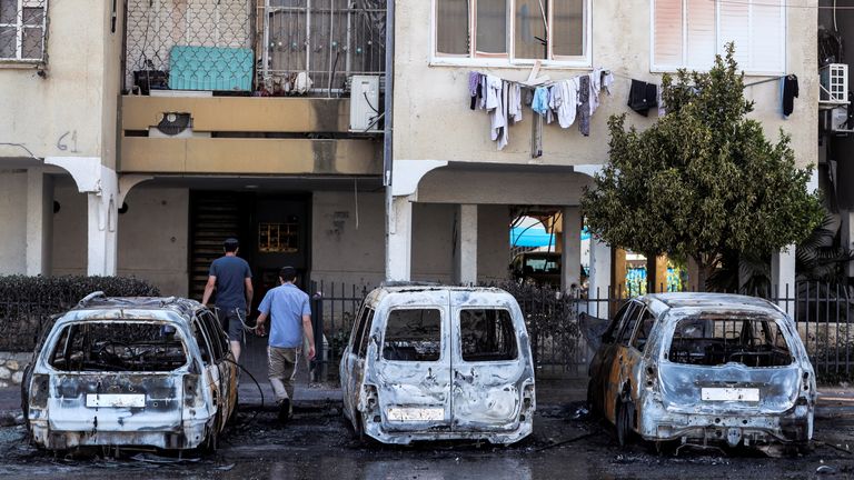 People walk next to burnt vehicles as they enter a building after violent confrontations in the city of Lod, Israel between Israeli Arab demonstrators and police, amid high tensions over hostilities between Israel and Gaza militants and tensions in Jerusalem May 12, 2021