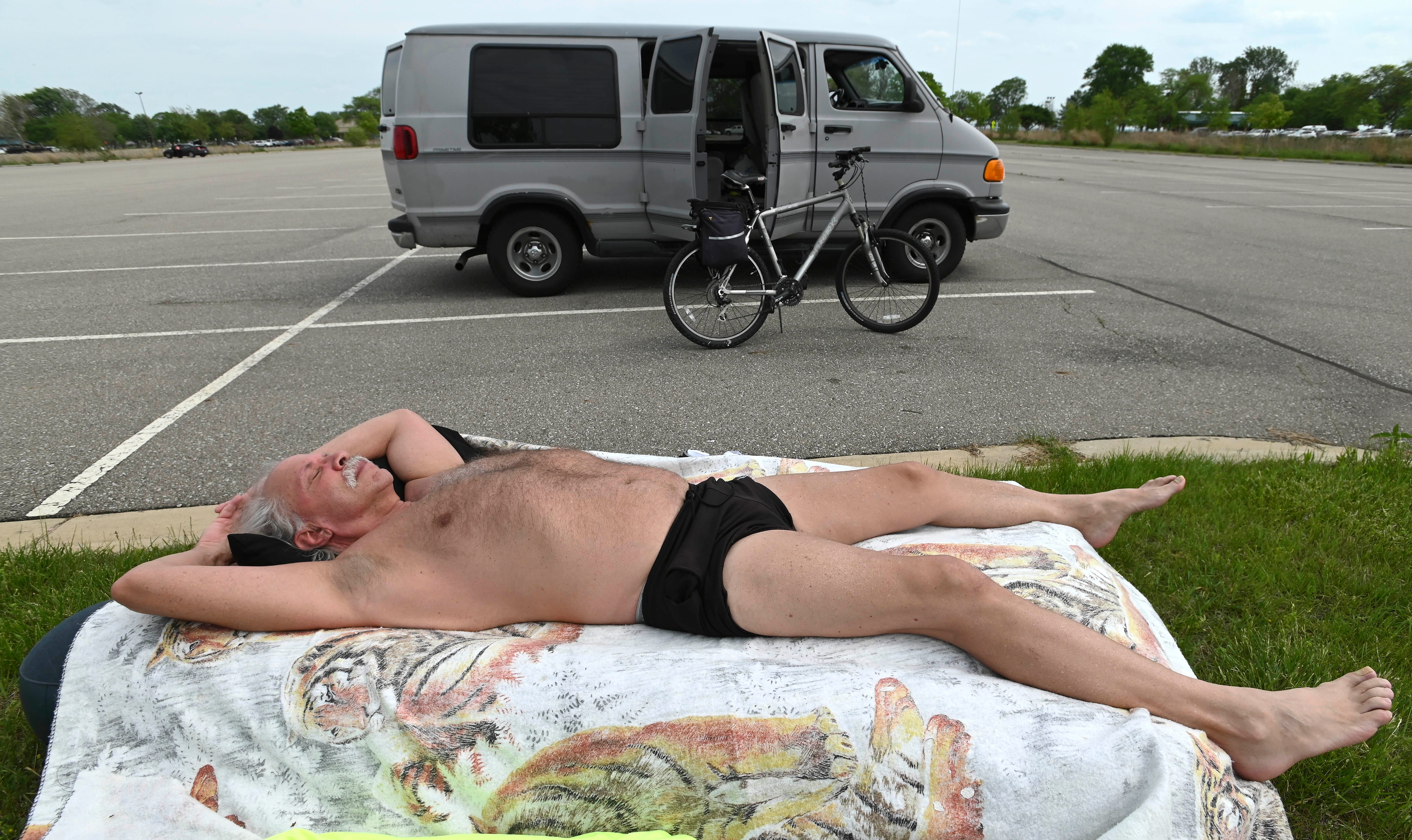 With temperatures in the mid to high 80s in Southeast Michigan, Joshua James of Macomb County sunbathes before riding his bike at Lake St. Clair Metropark in Harrison Township Tuesday afternoon, May 25, 2021.