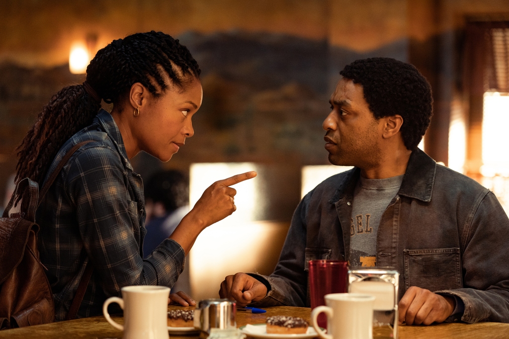 Naomie Harris and Chiwetel Ojiofor in a scene from the Showtime version of "The Man Who Fell to Earth." She's pointing at him as they sit at a table with two coffee mugs in front of them.