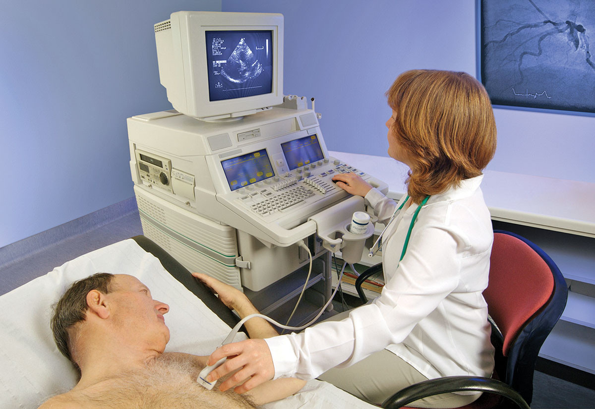 photo of a technician conducting an echocardiogram procedure on a patient, looking at a screen as she holds the sensor over the patient's heart