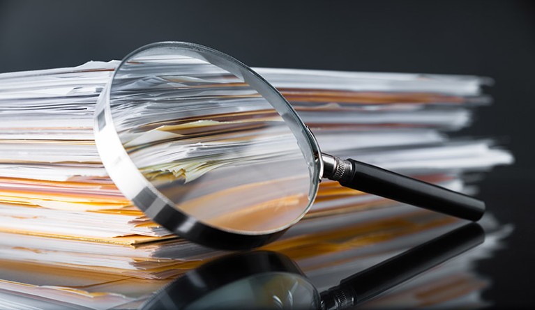 A magnifying glass leans against a stack of paper documents.