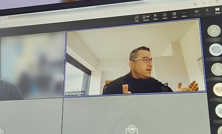 A man in a black shirt gestures as he speaks on a video call.